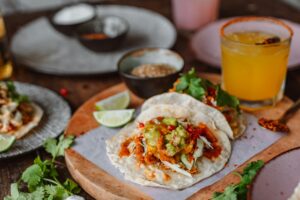 Delicious Mexican tacos with fresh guacamole, lime, and chili on a rustic wooden board.