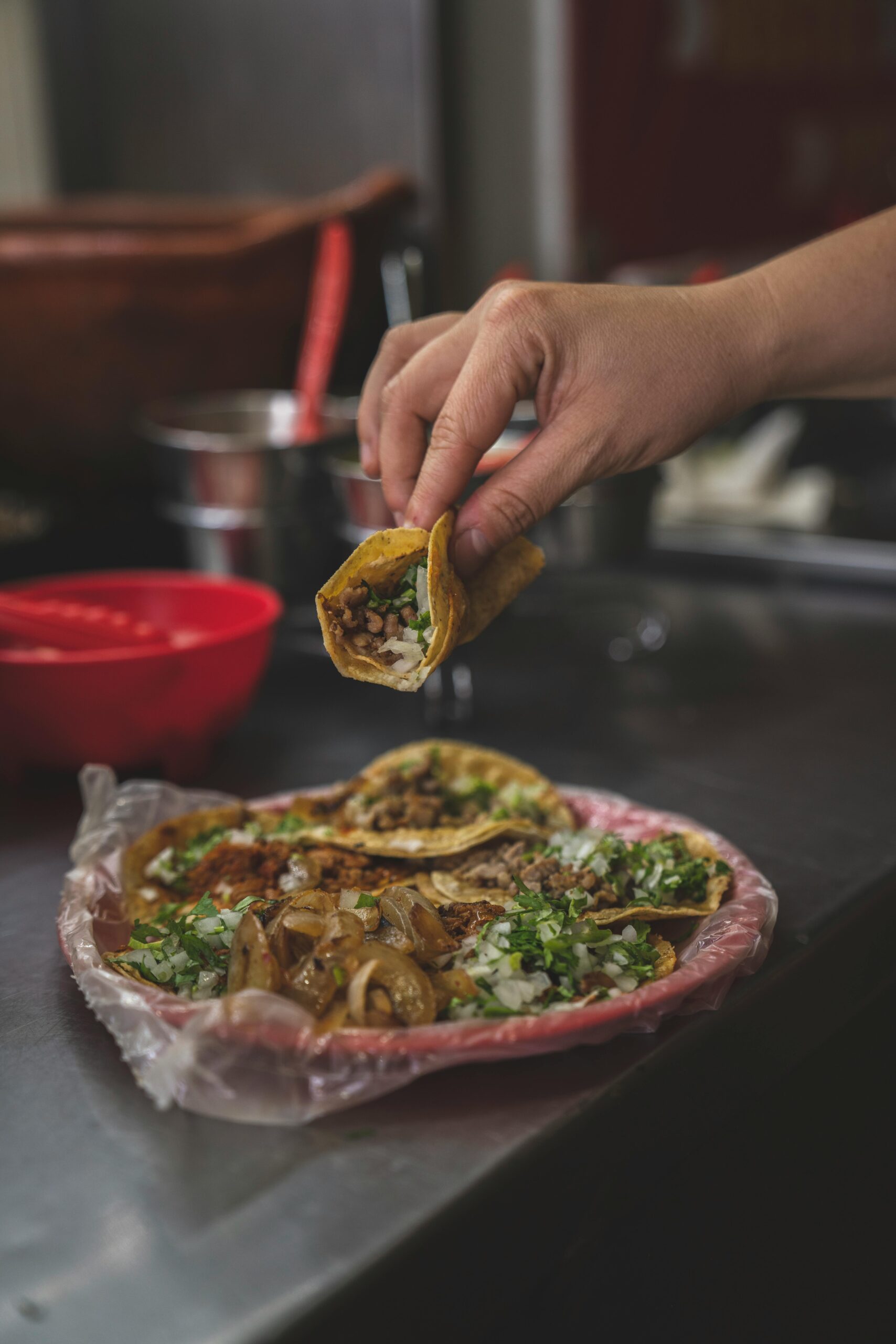 Close-up of a hand holding a delicious taco with a plate of assorted tacos in the background.